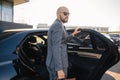 Portrait of a handsome businessman in sunglasses standing near the car outdoors in front of the modern building facade Royalty Free Stock Photo