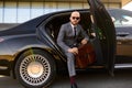 Portrait of a handsome businessman in sunglasses standing near the car outdoors in front of the modern building facade Royalty Free Stock Photo