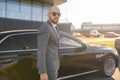 Portrait of a handsome businessman in sunglasses standing near the car outdoors in front of the modern building facade Royalty Free Stock Photo