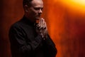 Portrait of handsome catholic priest or pastor with dog collar, dark red background.