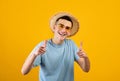 Portrait of handsome Caucasian man in straw hat and sunglasses pointing at camera on orange studio background Royalty Free Stock Photo