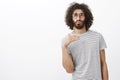 Portrait of handsome charming guy with bed behaviour, standing over gray background, whisteling and waving palm while