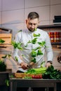 Portrait of handsome chef cooking salad in the kitchen. The cook cuts fresh green leaves of cabbage, spinach, arugula for Royalty Free Stock Photo