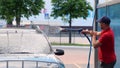 Portrait of handsome concentrated man in cap and red t-shirt washing his car outdoors using high pressure water. Guy Royalty Free Stock Photo