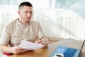 Portrait of handsome confident businessman sitting at wood desk and working with documents and laptop in modern office, copy space Royalty Free Stock Photo