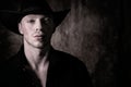 Portrait of handsome cowboy wearing black shirt with stetson hat looking at camera