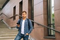 Portrait of handsome delivery man with large thermo backpack holding using mobile phone standing on stairs of office Royalty Free Stock Photo