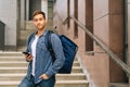 Portrait of handsome delivery man with large thermo backpack holding using mobile phone standing on stairs of office Royalty Free Stock Photo