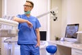 Portrait of a handsome dentist wearing a blue uniform, standing in a dentist clinic.