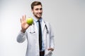 Portrait of handsome doctor in white coat looking at camera and smiling while holding an apple,  on white. Royalty Free Stock Photo