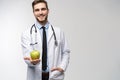 Portrait of handsome doctor in white coat looking at camera and smiling while holding an apple,  on white. Royalty Free Stock Photo