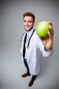 Portrait of handsome doctor in white coat looking at camera and smiling while holding an apple,  on white. Royalty Free Stock Photo