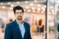 Portrait of handsome fashionable bearded young man in stylish suit and glasses looking at camera standing in hall of Royalty Free Stock Photo