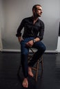 Portrait handsome fashionable man in a black shirt sits on a chair in a photo studio loft. Royalty Free Stock Photo