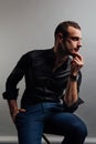 Portrait handsome fashionable man in a black shirt sits on a chair in a photo studio loft. Royalty Free Stock Photo