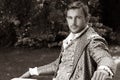 Portrait of handsome gentleman dressed in vintage costume sitting on bench in garden