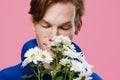 portrait of a handsome, guy with freckles on his face, in a blue sweater, sniffing a bouquet of large white daisies