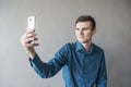 Portrait of a handsome guy looking into the camera with a phone in his hand. The guy makes self photo. In a green shirt. Brunette Royalty Free Stock Photo