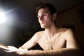 Portrait of a handsome guy with a naked torso. Photo of a close-up in a dark room and light from a lamp. Soft light. Green-eyed br Royalty Free Stock Photo