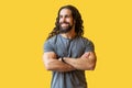 Portrait of handsome happy bearded young man with long curly hair in grey tshirt standing with crossed arms and looking away with Royalty Free Stock Photo