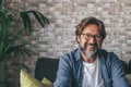 Portrait of handsome happy mature man looking at camera and smiling in the living room of modern apartment. Confident guy with Royalty Free Stock Photo