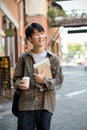 Handsome Asian male college student with a coffee cup and his school book walking in the campus Royalty Free Stock Photo