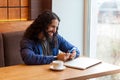 Portrait of handsome intelligence young bearded man freelancer in casual style sitting, holding his smartphone and looking with Royalty Free Stock Photo