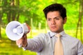 Portrait of a handsome mad man holding in his hand a megaphone, in a blurred green background