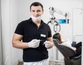 Portrait of handsome male dentist holding dental tools - probe and mirror at dental office. Dentistry