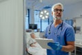 Portrait of handsome male doctor, patient in hospital bed behind. ER doctor examining senior patient, reading her Royalty Free Stock Photo