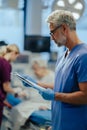 Portrait of handsome male doctor, patient in hospital bed behind. ER doctor examining senior patient, reading her Royalty Free Stock Photo