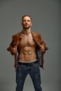 Portrait of a handsome male model posing shirtless in a brown leather jacket and jeans. Grey background. Fashionable Royalty Free Stock Photo