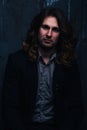 Portrait of a handsome man in a black jacket with long hair on a dark background, serious facial expression Royalty Free Stock Photo