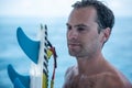 Portrait of handsome man with blue eyes, surfer holding surf board with blue fins and blue ocean Royalty Free Stock Photo