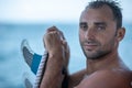 Portrait of handsome man with blue eyes, surfer holding surf board with blue fins and blue ocean Royalty Free Stock Photo