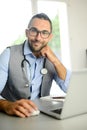 Portrait of handsome man male doctor in medical practice office writing prescription in laptop computer Royalty Free Stock Photo