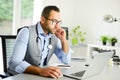 Portrait of handsome man male doctor in medical practice office writing prescription in laptop computer Royalty Free Stock Photo