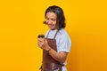 Portrait of handsome man wearing apron looking at cup of coffee being held isolated on yellow background