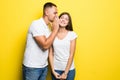 Portrait of handsome man whispering secret or interesting gossip to young woman in her ear isolated over yellow background