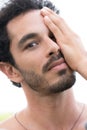 Close up portrait of healthy man with black hair, strong features, looking into the camera with hand covering one half of face