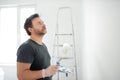 Portrait of a handsome mature man making repairs in the apartment. The person paints the wall white with roller. Do it yourself.