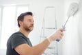 Portrait of a handsome mature man making repairs in the apartment. The person paints the wall white with roller. Do it yourself.