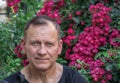 Handsome mature man 60 years old, in a black T-shirt, against a background of bright red flowers with a backpack Royalty Free Stock Photo