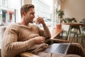 Portrait of handsome modern man, sitting in coffee shop with laptop, looking at screen with happy face, drinking Royalty Free Stock Photo