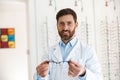 Portrait of handsome ophthalmologist offering glasses to client in optics store