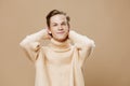 portrait of a handsome, pleasant guy on a plain background in a beige textured sweater, putting his hands behind his