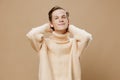 portrait of a handsome, pleasant guy on a plain background in a beige textured sweater, putting his hands behind his