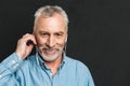 Portrait of handsome pleased mature man 60s with gray hair looking on camera while listening to music via white Royalty Free Stock Photo