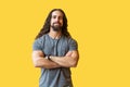 Portrait of handsome satisfied bearded young man with long curly hair in grey tshirt standing with crossed arms and looking at Royalty Free Stock Photo