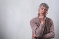 A portrait of handsome senior man standing near white wall dreaming about something looking aside holding his hand under his chin. Royalty Free Stock Photo